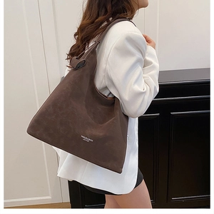 Detail of a dark brown matte leather tote bag worn by a model in chic urban office attire