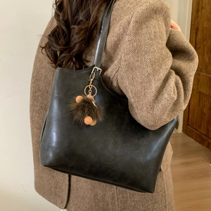 Detalle de un bolso tote de cuero negro mate con pompón marrón y el logo FASHION