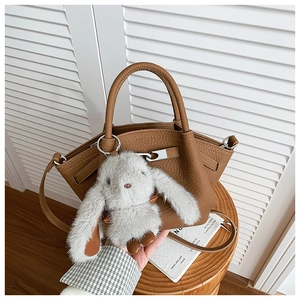 Detail view of brown lychee grain leather bucket bag with a cute grey bunny plush charm
