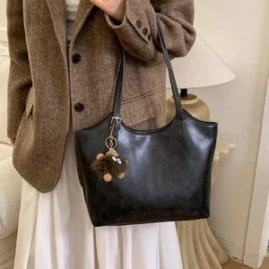 Detalle de bolso tote de cuero sintético negro con colgante de peluche y correa ajustable