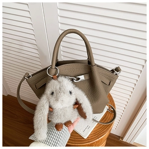 Detail of khaki lychee grain leather bucket bag featuring silver lock and plush bunny charm