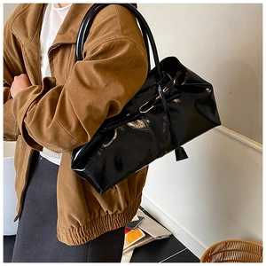 Close-up of black glossy patent leather tote bag with elegant side pendant detail