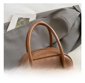Detail view of brown leather pillow bag featuring dual handles and metallic zipper hardware