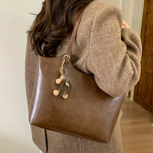 Detalle de bolso tote marrón vintage con colgante peludo sobre abrigo de espiga
