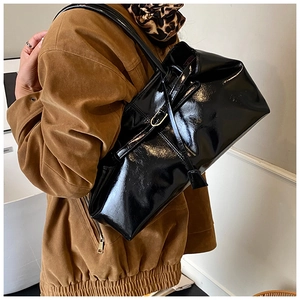Detail of glossy black patent leather tote bag styled with a brown jacket and scarf