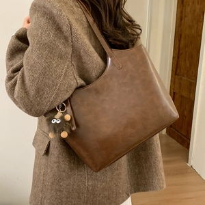 Bolso tote vintage de cuero sintético marrón con colgante de peluche sobre abrigo