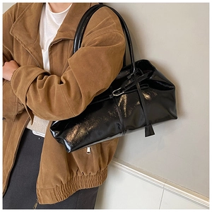 Model wearing a black glossy patent leather shoulder bag with a vintage minimalist style