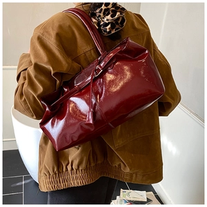 Detail of burgundy glossy leather tote bag showing shiny texture and long shoulder strap