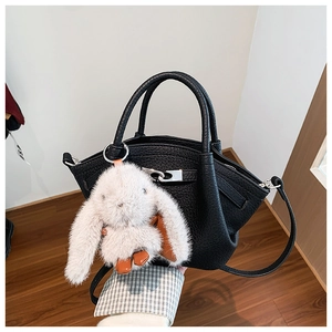 Detail of black lychee grain bucket bag with metal buckle and plush bunny charm