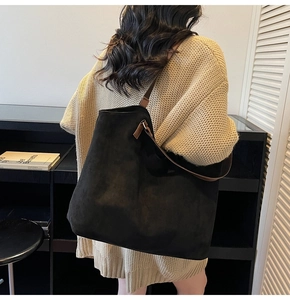 Modèle portant un grand sac cabas en daim noir avec des anses en cuir marron pour femme