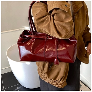 Close-up of a burgundy patent leather tote bag with glossy finish and metal buckle detail