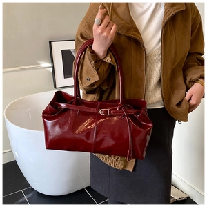 Detail of burgundy patent leather tote bag featuring a shiny finish and gold buckle strap