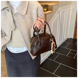 Close-up of deep brown Boston handbag featuring colorful wooden bead charm and zip closure