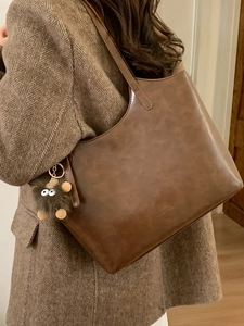 Bolso tote de cuero mate marrón oscuro con colgante de monstruo de peluche sobre abrigo