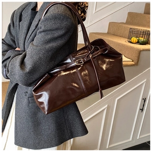 Detail of dark brown glossy leather tote bag shown with shoulder strap and buckle accent