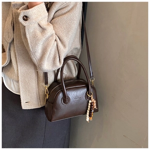 Detail of dark brown leather baguette bag with bead tassel and gold metal hooks