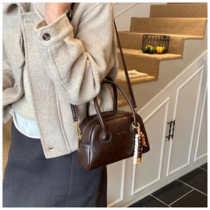 Detail of dark brown leather bowling bag with top handles and beaded charm accessory