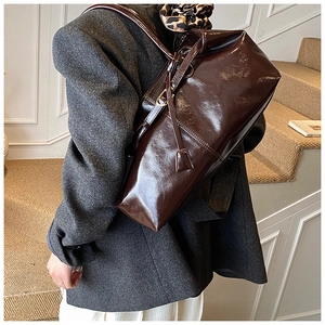 Detail of dark brown glossy patent leather tote bag with slim straps and metal accents