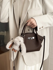 Dark brown leather bucket bag with silver lock and fluffy rabbit charm held by model
