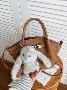 Brown lychee leather bucket bag with plush rabbit pendant on wooden stool