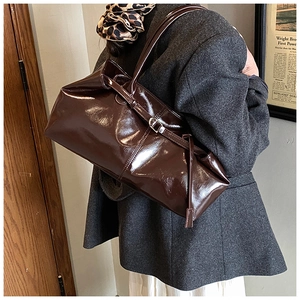 Brown gloss leather shoulder bag worn by model with grey suit and white skirt