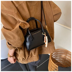 Close-up of black matte baguette bag with dual handles and bohemian beaded charm detail