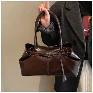 Close-up of brown glossy patent leather tote bag with pleated details and metal buckle