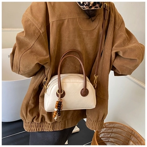 Close-up of retro cream pillow bag with wooden bead charm and brown leather handles