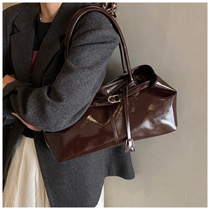 Detail of glossy dark brown patent leather tote bag with metallic buckle and strap