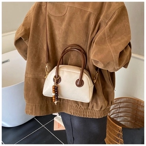 Detail of cream vintage boston bag with brown handles and bead tassel on a model
