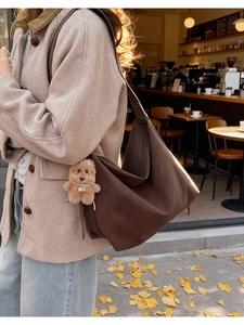 Dettaglio della borsa tote marrone caffè con ciondolo a orsetto su una modella all'aperto