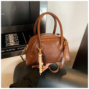 Detail of a brown vintage leather handbag with beaded charm and embossed brand logo