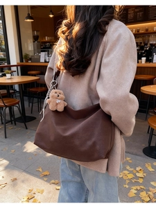 Dettaglio borsa tote in pelle scamosciata marrone scuro con ciondolo a orsetto in un caffè