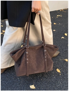 Detail of dark brown suede tote bag with decorative silver buckle straps in autumn setting