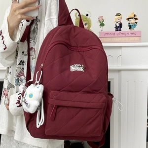 Nahaufnahme des weinroten gesteppten Nylon-Rucksacks mit Reißverschluss und Katzenanhänger