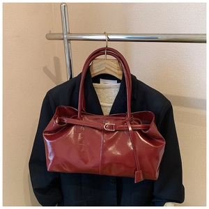 Detail of dark red glossy patent leather tote bag with metallic buckle and slim straps