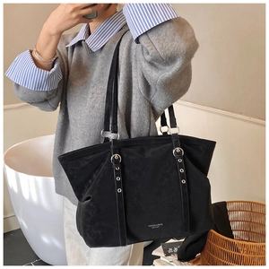 Detail of a large black tote bag featuring silver buckle straps and a textured matte finish