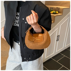 Detail of brown suede crescent bag with brand logo and heart pendant charm