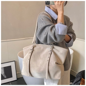 Mirror selfie showing a beige tote bag with twin metal buckles and slim shoulder straps