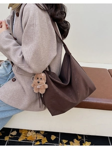 Dettaglio della borsa tote in pelle marrone scuro con tracolla larga e peluche