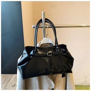 Close-up of black glossy patent leather shoulder bag with pleats and buckle detail