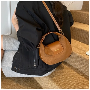 Detail of a brown crescent bag with suede stitching and a heart pendant in a lifestyle setting