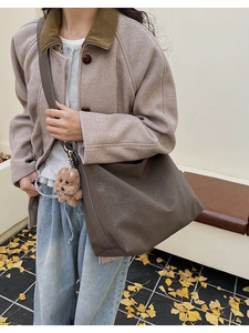 Dettaglio borsa tote in pelle marrone con ciondolo a orsetto su sfondo autunnale