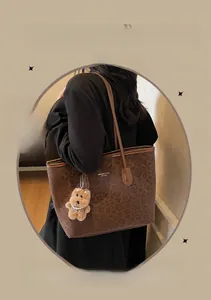 Leopard print tote bag detail with brown shoulder strap and fuzzy bear charm accessory