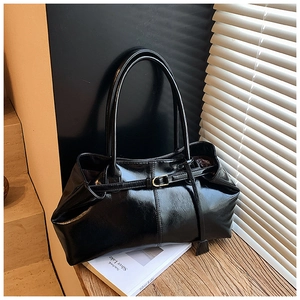 Detail of black patent leather tote bag with buckle decor on a wooden desk setting