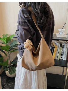 Detailed view of brown PU tote bag featuring a cute plush bear charm on wide shoulder strap