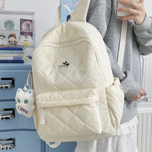 Seitenansicht des cremefarbenen gesteppten Rucksacks mit Rautenmuster und süßem Plüschtier
