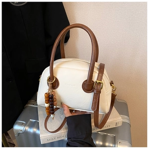 Detail view of a vintage cream leather Boston bag with wooden bead charm on a suitcase