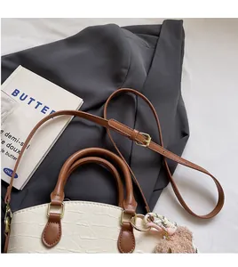 Detail of white crocodile texture handbag with adjustable brown strap and bear charm