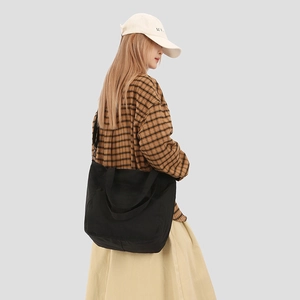 Black canvas tote bag styled as a crossbody messenger bag on a female model